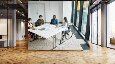 Wide angle view at diverse business team discussing project at meeting table with focus on young woman in wheelchair Wall mural