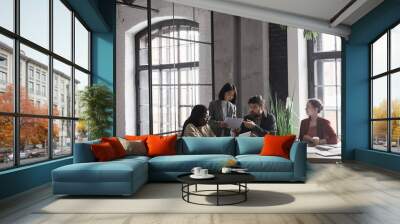 Wide angle view at multi-ethnic group of business people discussing project while sitting at meeting table in graphic office interior, copy space Wall mural