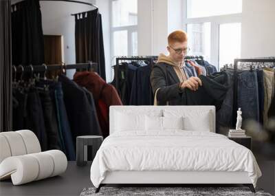 Wide angle view of young man browsing clothes on racks while shopping sustainably in thrift shop Wall mural