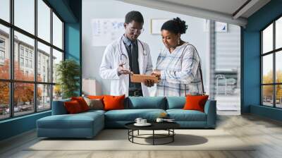 Young black doctor consulting female patient using digital tablet in clinic Wall mural