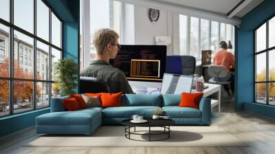 Young programmers writing codes on computer sitting at their workplace during working day in IT office Wall mural