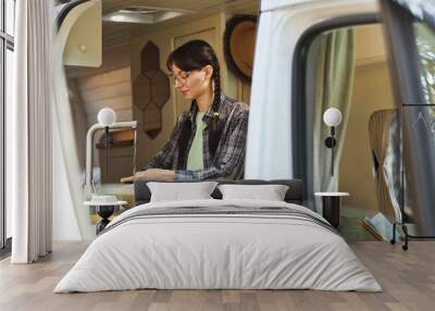 Young woman in eyeglasses washing vegetables under water in sink while standing in the van during camping Wall mural