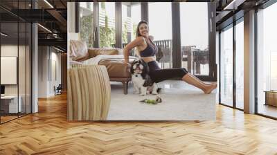 Middle age Brazilian woman in sportswear doing home exercise triceps dips workout with her dog, making video call, online yoga fitness class concept Wall mural