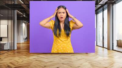 Amazed young Asian woman with open mouth holding head with two a hands on purple background Wall mural