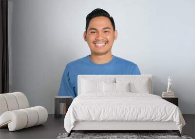 Portrait of happy young Asian man in blue t-shirt looking at camera with smiling face isolated on white background Wall mural