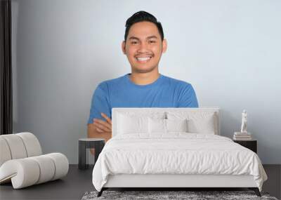 Portrait of happy young Asian man in blue t-shirt standing with crossed arms, smiling at camera, looking confident isolated on white background Wall mural