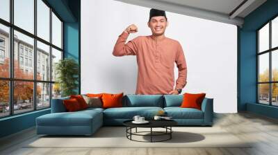 Smiling Asian Muslim man raises arms and showing muscle isolated over white background Wall mural