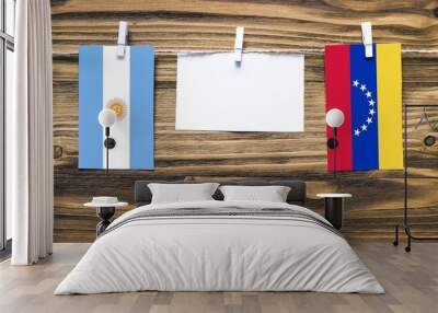 Hanging flags of Argentina and Venezuela attached to rope with clothes pins with copy space on white note paper on wooden background.Diplomatic relations between countries. Wall mural