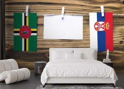 Hanging flags of Dominica and Serbia attached to rope with clothes pins with copy space on white note paper on wooden background.Diplomatic relations between countries. Wall mural