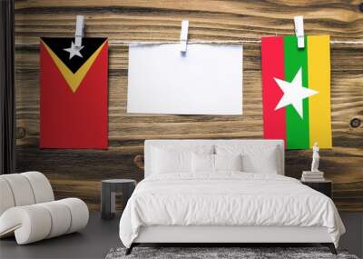 Hanging flags of East Timor and Myanmar attached to rope with clothes pins with copy space on white note paper on wooden background.Diplomatic relations between countries. Wall mural