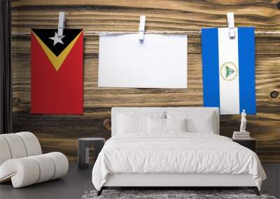 Hanging flags of East Timor and Nicaragua attached to rope with clothes pins with copy space on white note paper on wooden background.Diplomatic relations between countries. Wall mural