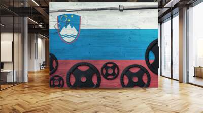 Slovenia gym concept. Top view of heavy weight plates with iron bar on national background. Wall mural