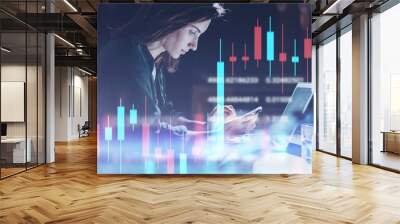 Business woman sitting at night office in front laptop computer and using her mobile phone. Red and green candlestick chart and stock trading computer screen background. Double exposure. Wide Wall mural