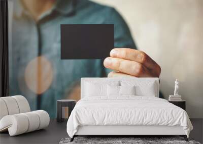 Man wearing blue jeans shirt and showing blank black business card. Blurred background. Horizontal mockup Wall mural