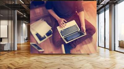 Photo of man sitting in studio on the floor, holding modern laptop hands and working with notebook. Blurred background. Horiontal Wall mural