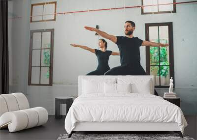 Young sportive man and woman are practicing yoga exercises in the studio. Couple of young sporty people practicing yoga lesson with partner. Wall mural