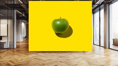 Green apple on a yellow background. Hard shadow, overhead. Wall mural