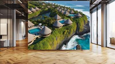 Aerial view of a coastal resort area featuring a series of thatched-roof villas and buildings nestled along a lush, green cliffside. Wall mural