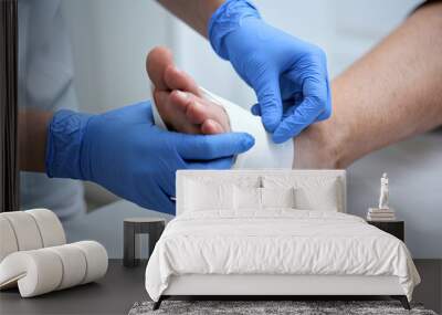 A nurse wearing blue gloves doing bandage on a wound on a person's foot Wall mural