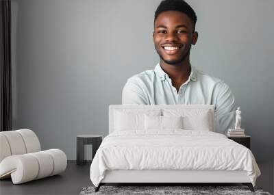 Confident young man in casual attire with arms crossed, flashing a friendly smile against a soft gray background. Wall mural