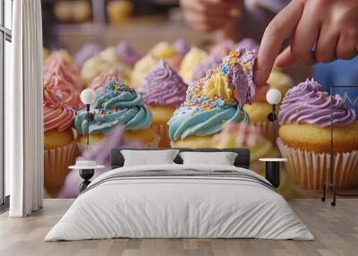 A closeup of a table full of colorful and decorated cupcakes. A baker is in the background, putting the finishing touches on the last cupcake. Wall mural