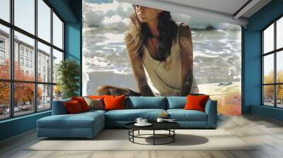 A woman is sitting on the beach with a surfboard next to her. She looks pensive, lost in thought. Wall mural