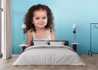 Curly haired toddler with secret smile isolated on blue background Wall mural