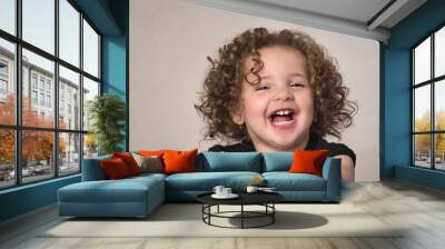 Laughing smiling happy toddler girl kid with curly brown hair isolated on beige background Wall mural