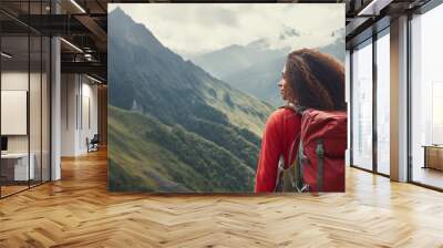 female hiker with a backpack looking at a beautiful view of high mountains under clear sky. Wall mural