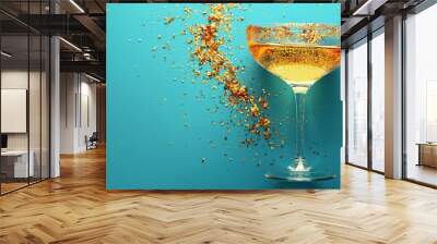   A close-up of a wine glass filled with liquid and sprinkles of gold against a blue background Wall mural