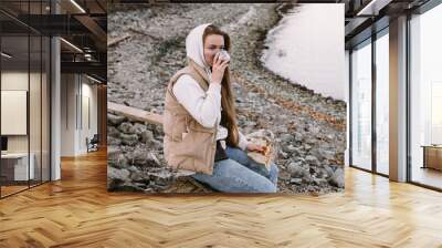 young woman drinking tea on river shore at autumn season Wall mural