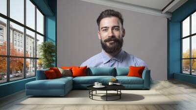 Horizontal  head and shoulder portrait of young bearded business man smiling at camera against gray studio background. Wall mural