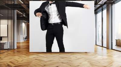 Young man putting on black suit tuxedo coat.  Full body length portrait over gray studio background. Wall mural