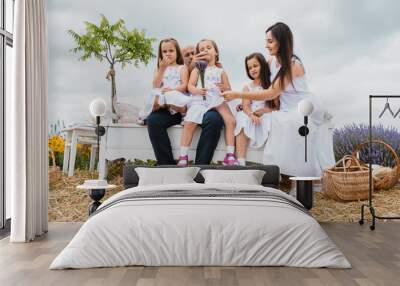 Family with three children sitting on the bench outdoors in a park talking chatting.Happy cheerful family on vacation. Mom, and three children are playing, hugging. Wall mural