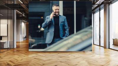 The man waits for a meeting near office. The businessman speaks by phone.Stylish man in a blue suit in the city. Business style of emotion. Wall mural