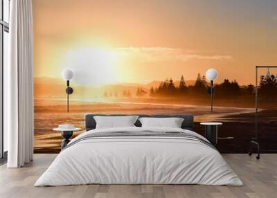 A large coral colored sunset above the calm beach in Gisborne, New Zealand. Wall mural