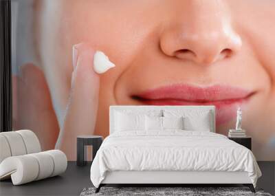 Beautiful young woman applying a creme on her face isolated on gray background Wall mural