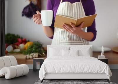 young woman reading cookbook in the kitchen, looking for recipe Wall mural