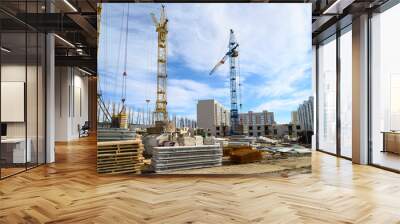 Photos of high-rise construction cranes and an unfinished house against a blue sky. Photographed on a wide angle lens. Wall mural