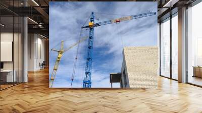 Photos of high-rise construction cranes and an unfinished house against a blue sky. Photographed on a wide angle lens Wall mural