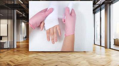 Young female hands wearing pink gloves wrapping gauze on young hand and wrist. Medical treatment. Wall mural