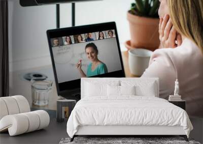 laptop on a work desk showing back view of a woman watching screen of a video conference, a speaker,many attendees, a team meeting or online coaching and worshop event  Wall mural