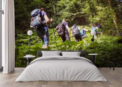 sporty group of people from behind while hiking through the forest surrounded by many green leaves Wall mural