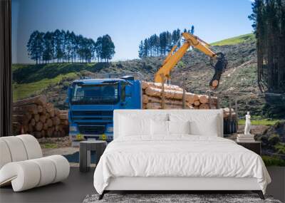 A blue log truck being loaded with logs by a swing loader Wall mural