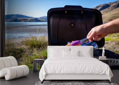 A man cooks bacon and eggs on a portable bbq beside the seaside on a sunny winter day travelling in New Zealand Wall mural