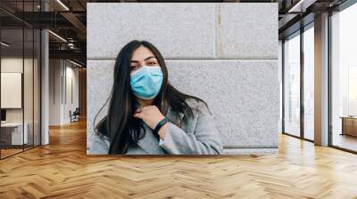 Portrait of a beautiful adult young woman against a gray wall in a medical face mask Wall mural