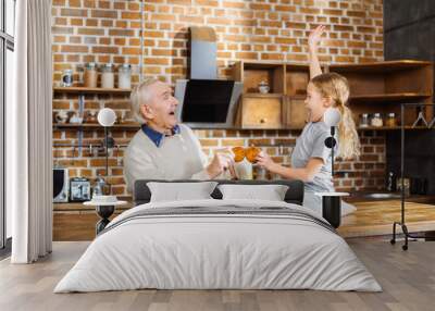 Joyful aged man eating home made pastry with his granddaughter Wall mural