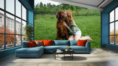 Beautiful woman hugging and kissing Irish Setter dog. Dog and owner together outdoors. Love and friendship between dog and owner in park. true friends forever, people pets concept Wall mural