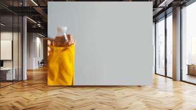 Young woman in white T-shirt takes out a plastic bottle of water from a yellow bag on a gray background Wall mural