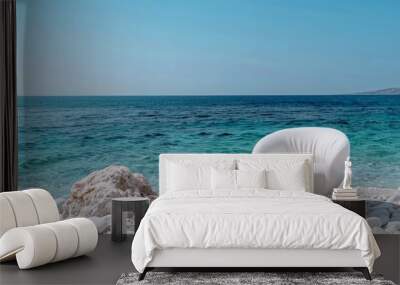 A chair on a white rock on the beach, Greece, has a clear blue sky and the Mediterranean Sea Wall mural